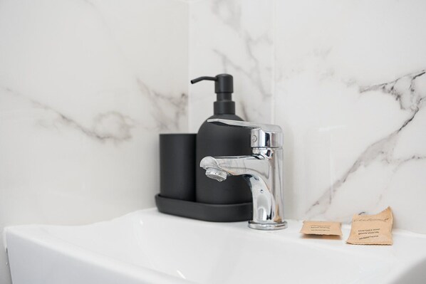 A modern bathroom with a white sink, a chrome faucet, and a black soap dispenser.