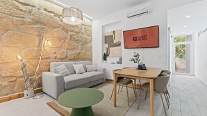 Un salon moderne avec un mur en pierre, un canapé gris, une table à manger en bois et une petite table d’appoint verte.