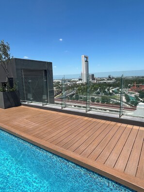 A rooftop pool with a view of a cityscape, including a tall building and a bridge.