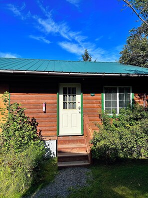 Una baita di legno con tetto verde, una porta bianca e un piccolo portico.