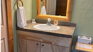 Ein Badezimmer mit einem Holzbadezimmerhocker, einem weißen Waschbecken, einem Spiegel und einem Handtuch, das an einem hölzernen Handtuchhalter hängt.