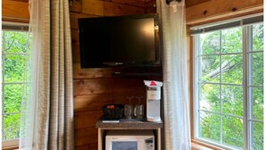 Ein Zimmer in einer Holzhütte mit Fernseher an der Wand, einer Kaffeemaschine und einer Mikrowelle auf einer Arbeitsplatte.