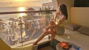 A woman sitting by a window overlooking a beach with umbrellas and lounge chairs. - HuiZhou The Ushuaia Resort (Huizhou)