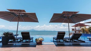 A poolside area with two lounge chairs and umbrellas, overlooking a body of water and distant mountains.