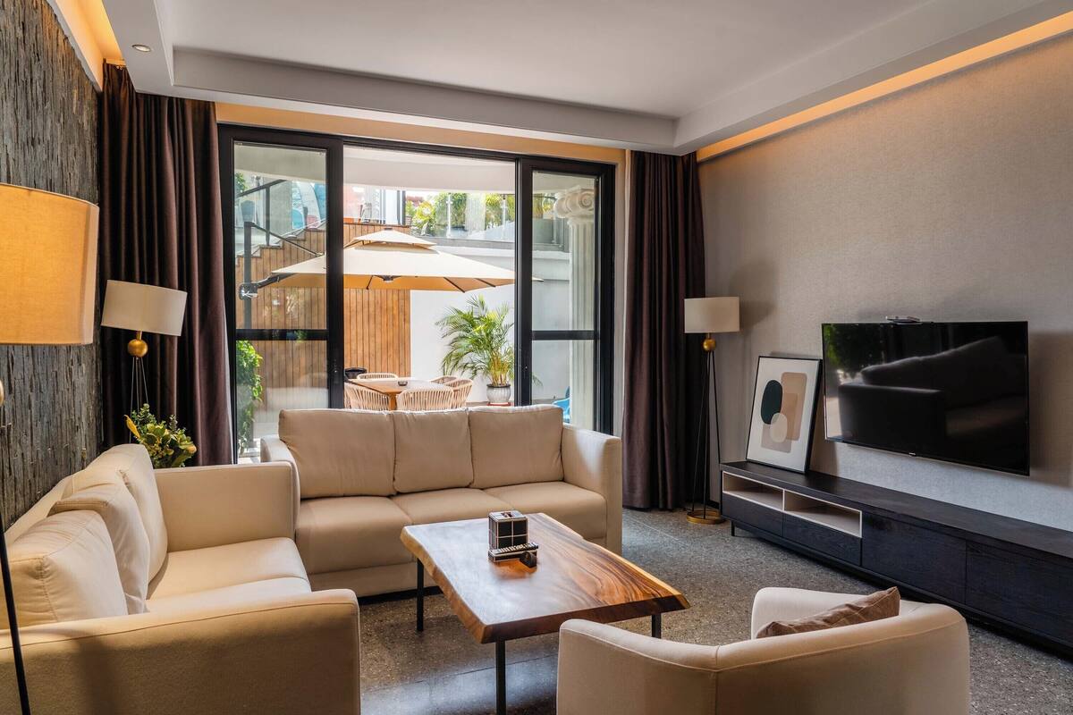A modern living room with a sofa, a coffee table, a TV, and a sliding glass door leading to an outdoor area.