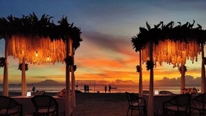 A beachside venue with a sunset view, featuring a long table with chairs and a swing set.