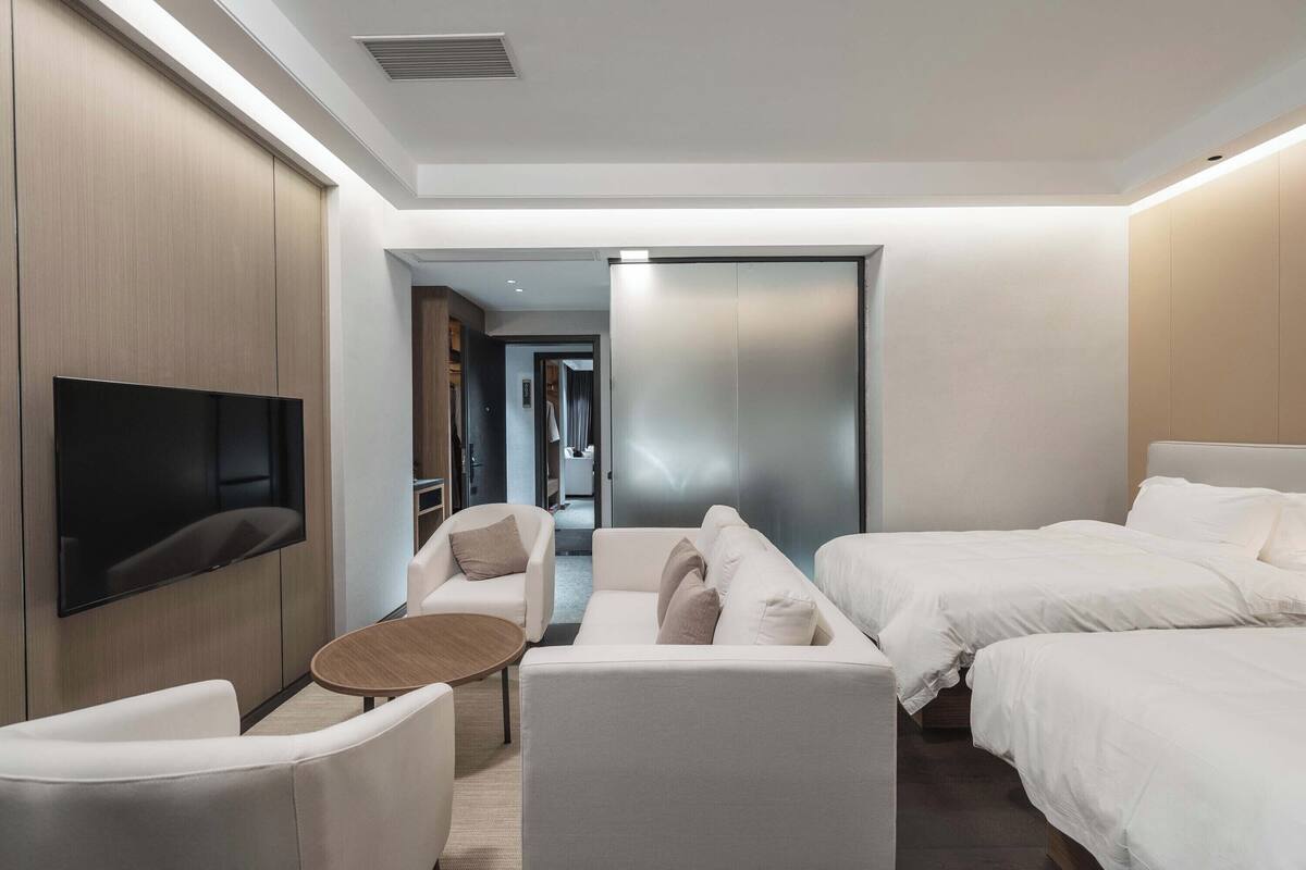 A modern hotel room with a flat-screen TV, a sofa, a small round table, and two beds.