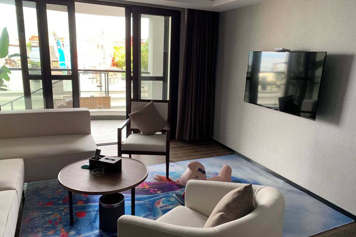 A modern hotel room with a large TV, a sofa, a chair, and a coffee table.