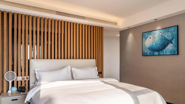 A modern hotel room with a large bed, wooden slat headboard, a bedside table with a lamp, and a wall-mounted artwork. - HuiZhou The Ushuaia Resort (Huizhou)