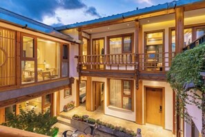 A two-story wooden building with balconies, large windows, and a well-lit interior. - UNThinkHotel Qimu inn (Lijiang)