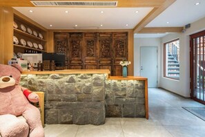 A reception area with a stone counter, wooden cabinets, and a large teddy bear. - UNThinkHotel Qimu inn (Lijiang)
