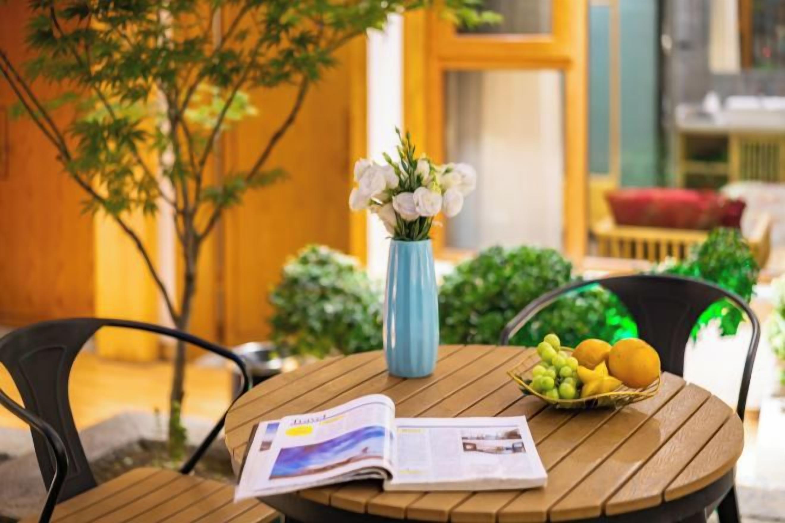 Une table en bois, un journal, un vase avec des fleurs blanches et un panier de fruits.