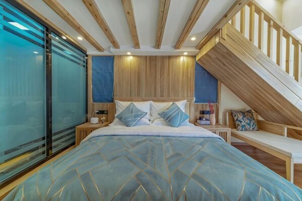 Une chambre avec un grand lit, des poutres apparentes en bois au plafond, un escalier et une porte en verre.