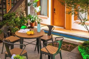 A round table with four chairs, a vase with flowers, and a potted plant on a patio. - UNThinkHotel Qimu inn (Lijiang)