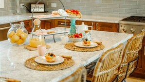 A kitchen with wooden cabinets, a marble island, wicker chairs, and a hanging light fixture. - Villa La Colina - Tierra Del Sol Mansion 3 minutes to BEACH, 4 BDRM 4.5 BTHRM (Tierra Del Sol)