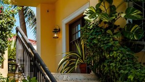 A staircase with a black railing leading to a door, surrounded by lush greenery and a yellow wall. - Villa La Colina - Tierra Del Sol Mansion 3 minutes to BEACH, 4 BDRM 4.5 BTHRM (Tierra Del Sol)