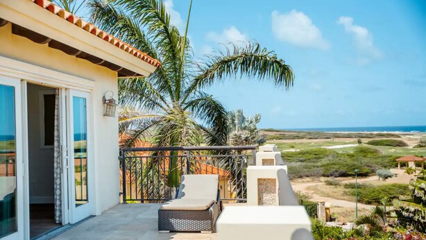 A balcony with a view of the ocean, palm trees, and a pathway leading to a building with a tiled roof. - Villa La Colina - Tierra Del Sol Mansion 3 minutes to BEACH, 4 BDRM 4.5 BTHRM (Tierra Del Sol)