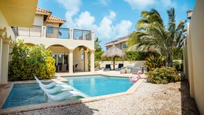 A pool area with a white lounge chair, a flamingo float, and a thatched umbrella. - Villa La Colina - Tierra Del Sol Mansion 3 minutes to BEACH, 4 BDRM 4.5 BTHRM (Tierra Del Sol)