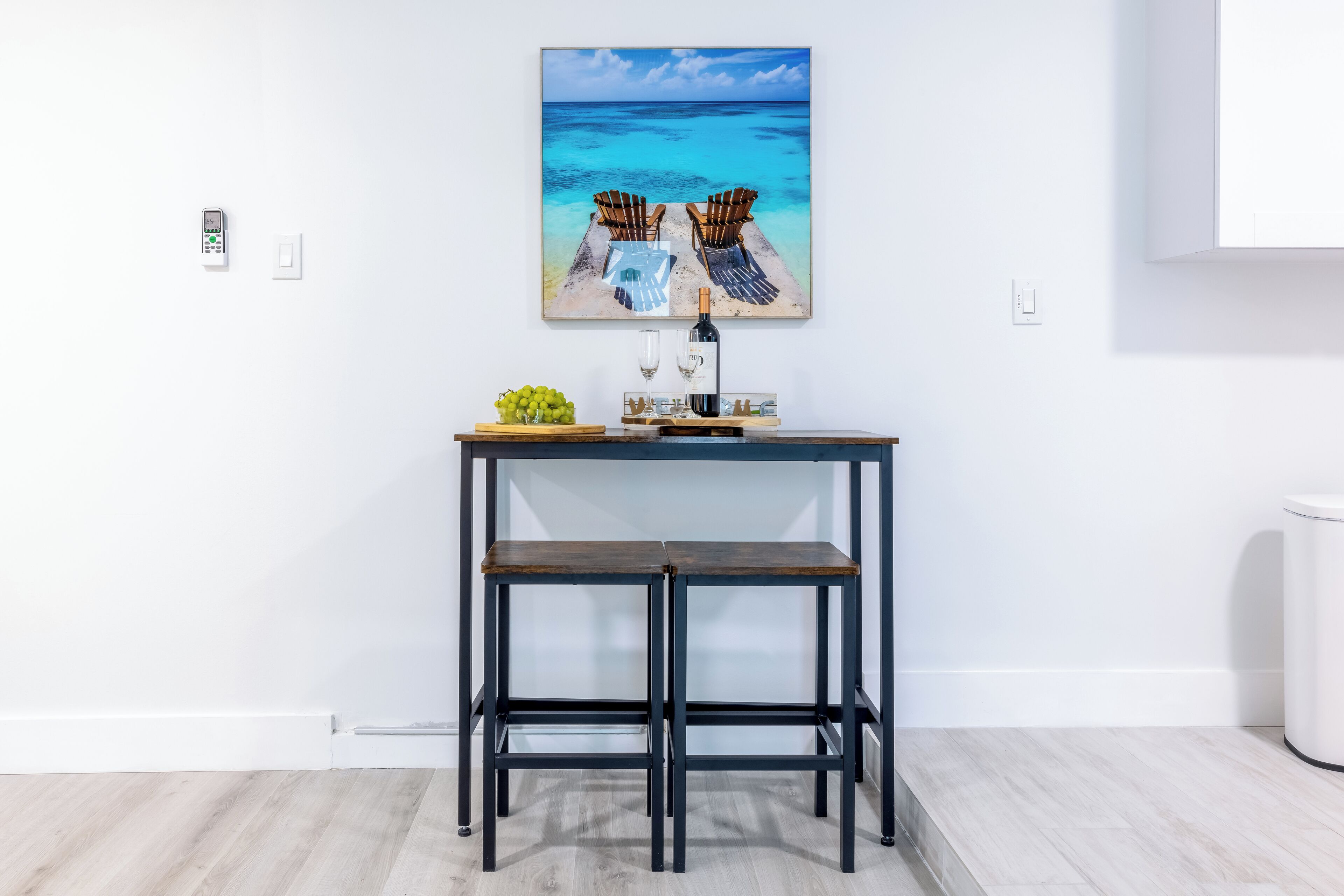 A modern kitchen with a wooden table, two chairs, a wine bottle, and a fruit bowl.