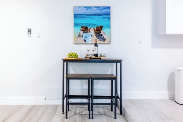 A modern kitchen with a wooden table, two chairs, a wine bottle, and a fruit bowl.