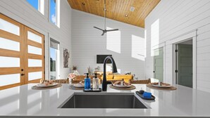 A modern kitchen with a central island, a ceiling fan, and a large window. - Ranch & Relax - Sauna, Hot Tub + Stargazing Escape (Broken Bow)