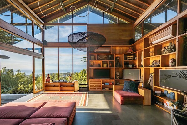 Amplia sala de estar con ventanas grandes, techo alto y varios estantes y muebles de madera.