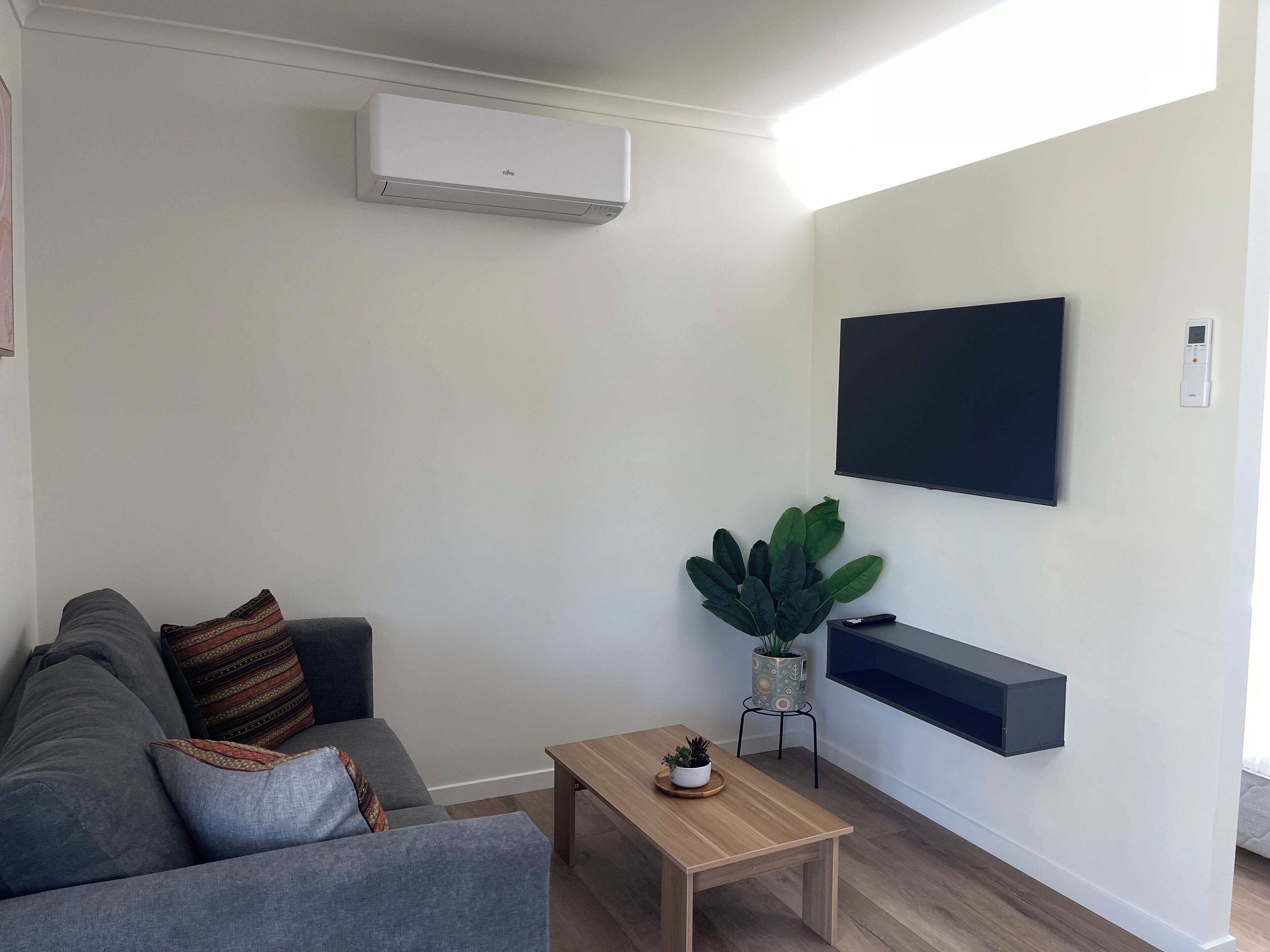 Un soggiorno moderno con un divano grigio, un tavolino in legno, una TV a parete e un condizionatore d'aria.