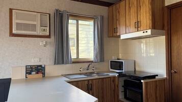 A compact kitchen with wooden cabinets, a microwave, a built-in oven, and a window with curtains.
