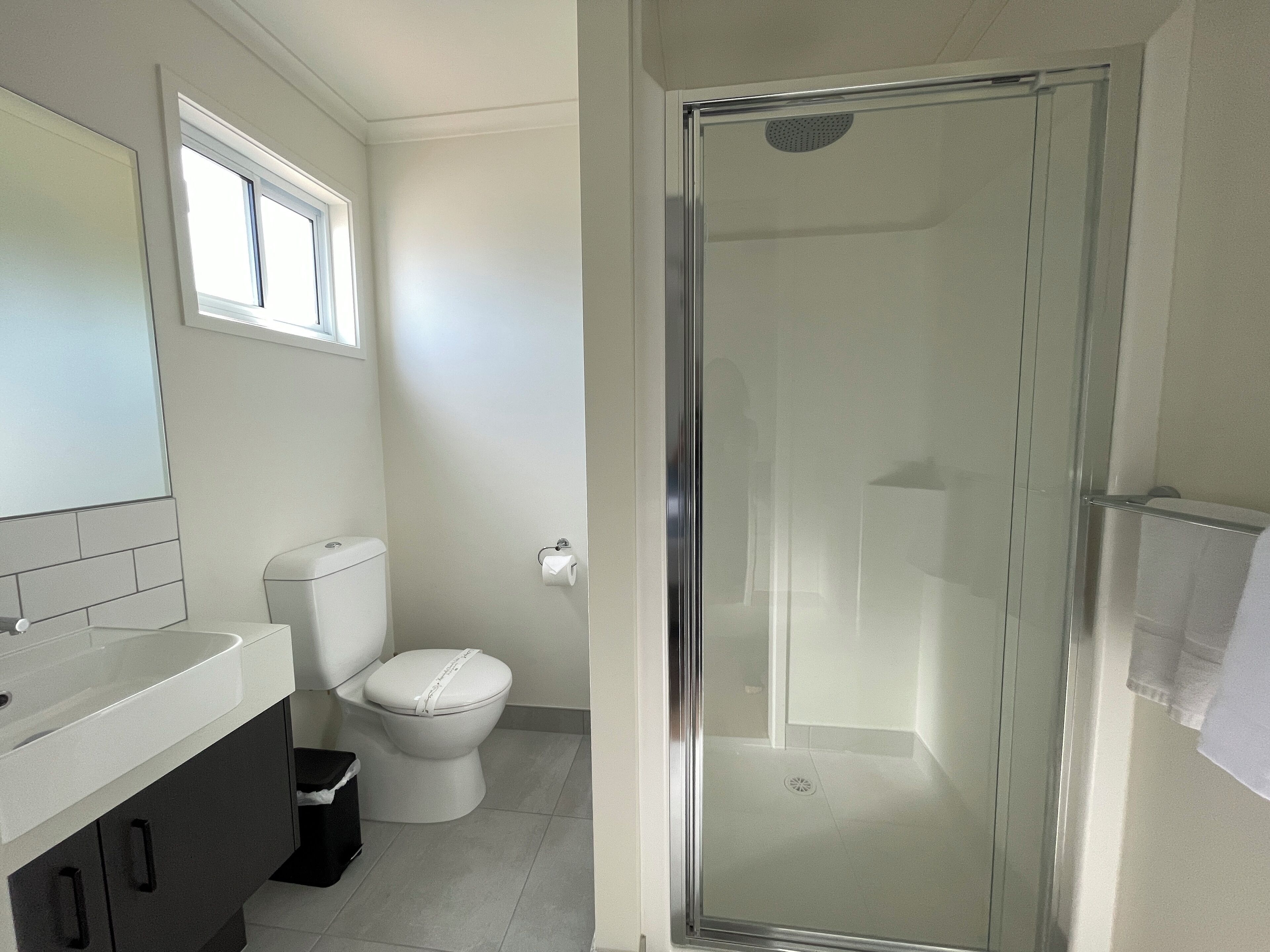 Un baño con inodoro, lavamanos, espejo y ducha con mampara de vidrio.