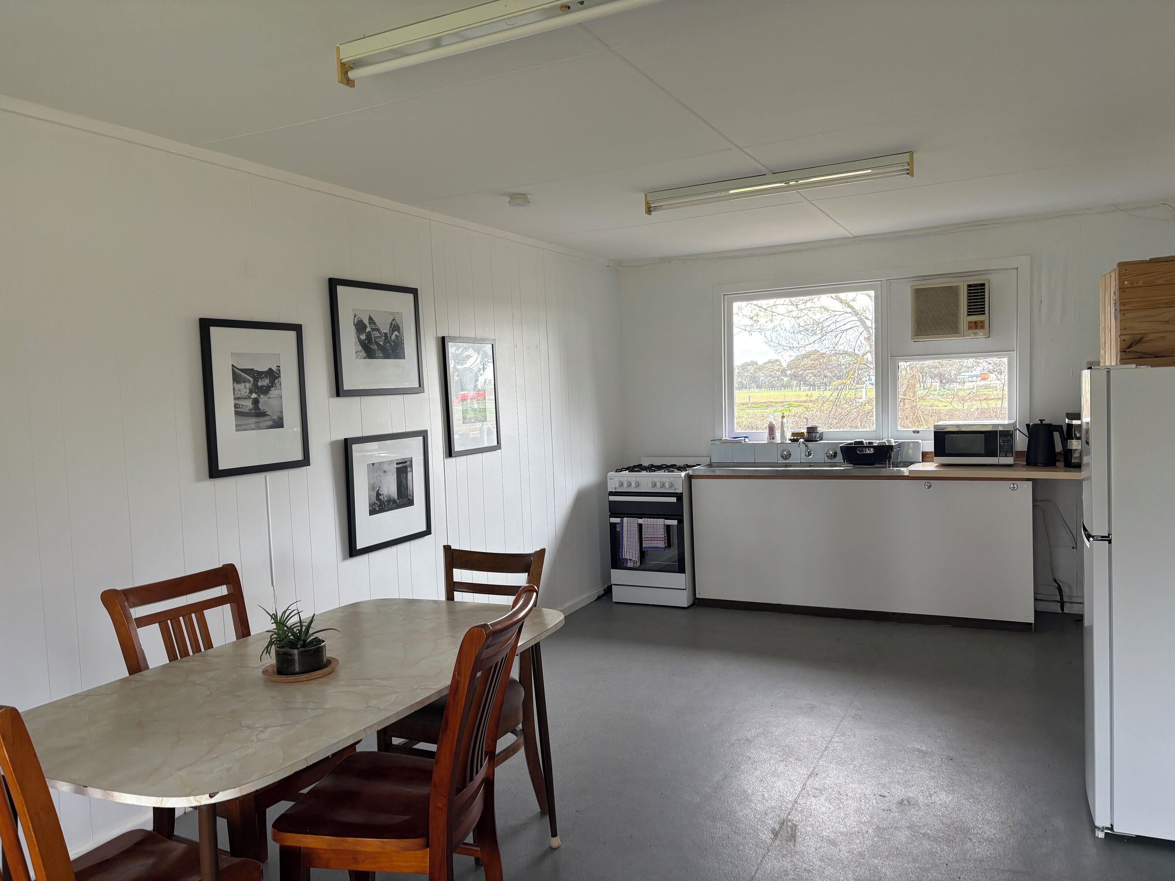 A kitchen with white cabinets, a stove, a microwave, and a refrigerator. There is a dining table with chairs and a potted plant.