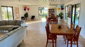 Un salón amplio con sofá, una mesa de comedor con sillas, una estantería y un gran ventanal con vistas a zonas verdes.