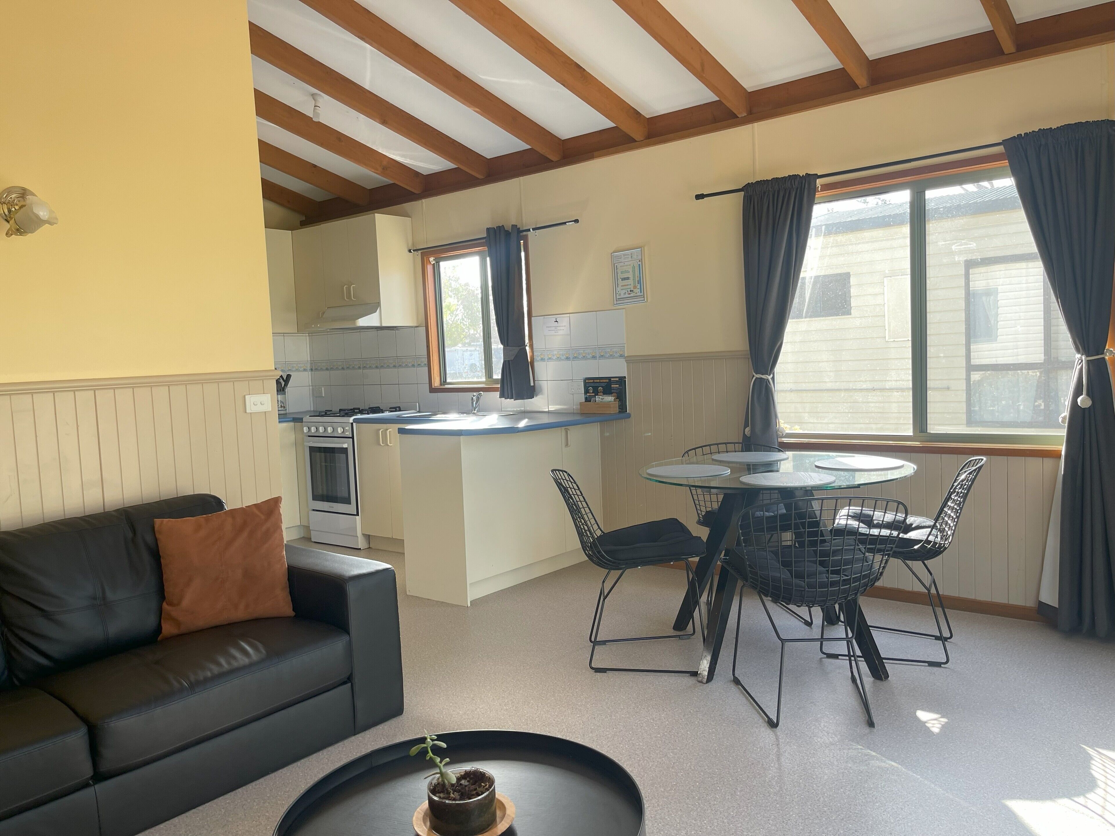 A compact kitchen with a dining area, a black leather sofa, and a small table with a potted plant.