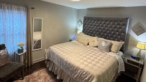A hotel bedroom with a large bed, a bedside table with a lamp, a chair, and a mirror. - Cozy Single-family house (Glendale)