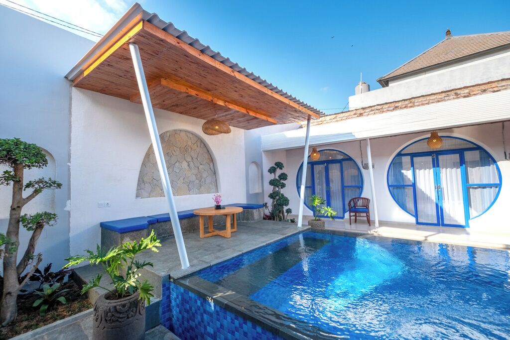 A swimming pool with a wooden pergola, a stone wall, and a small table with a chair.