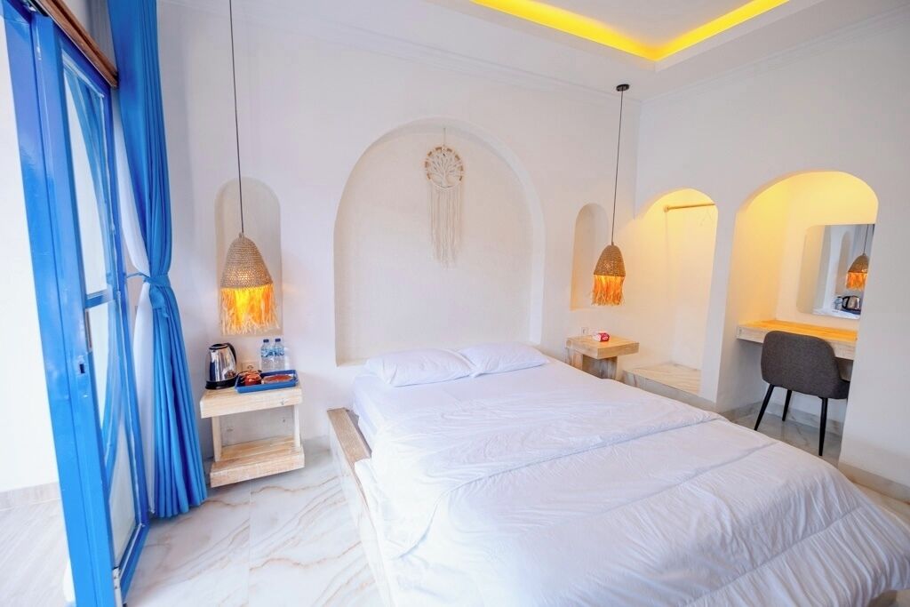 A hotel room with a large bed, a desk, and a chair. There are two pendant lights hanging from the ceiling.