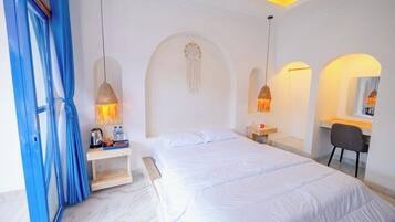 A hotel room with a large bed, a desk, and a chair. There are two pendant lights hanging from the ceiling.