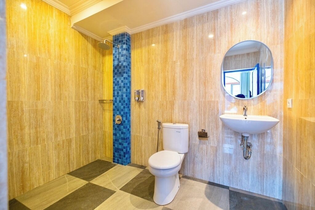 A modern bathroom with a checkered floor, a toilet, a sink with a mirror, and a shower area with a blue-tiled column.
