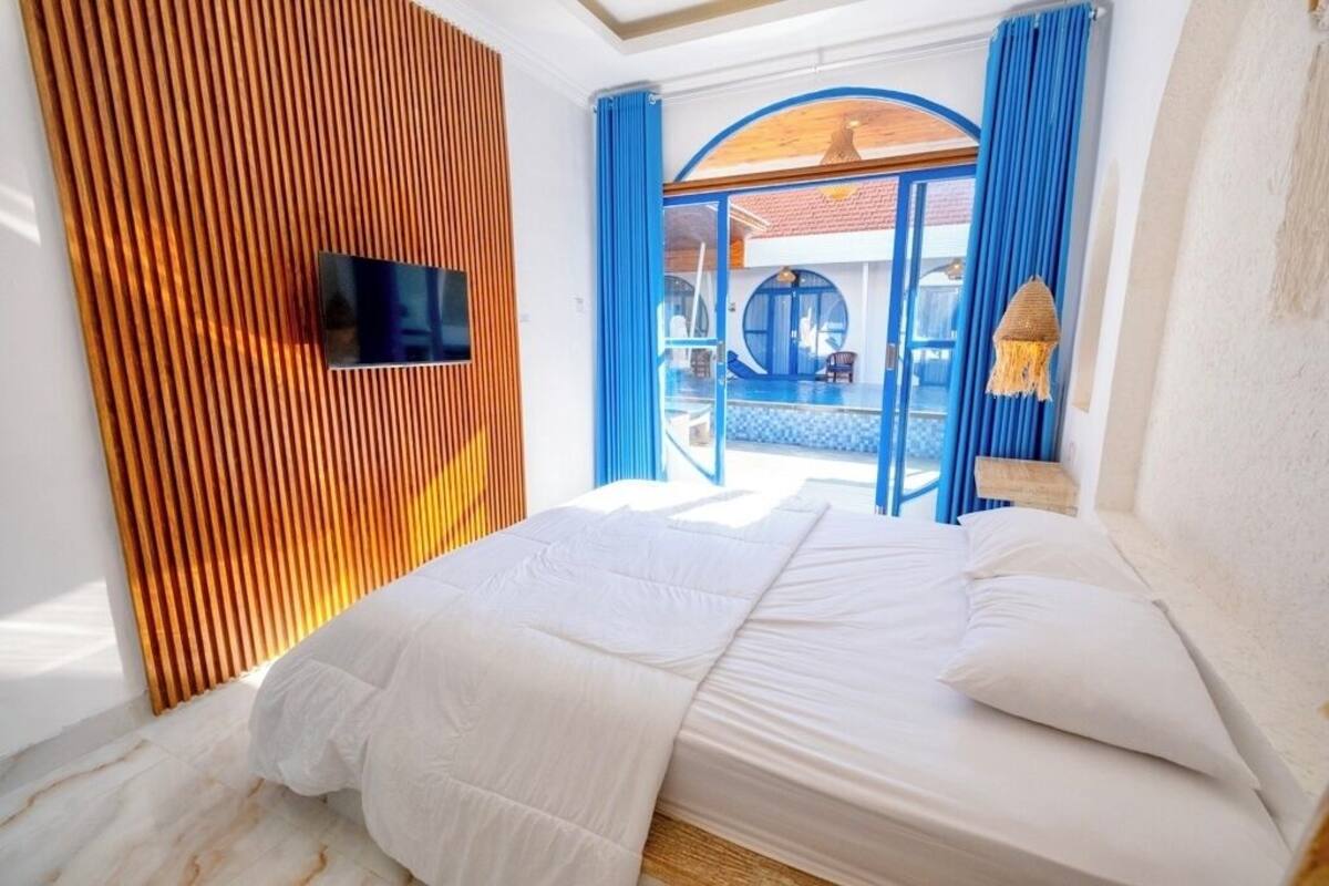 A bedroom with a bed, a TV mounted on the wall, and a view of a pool area.