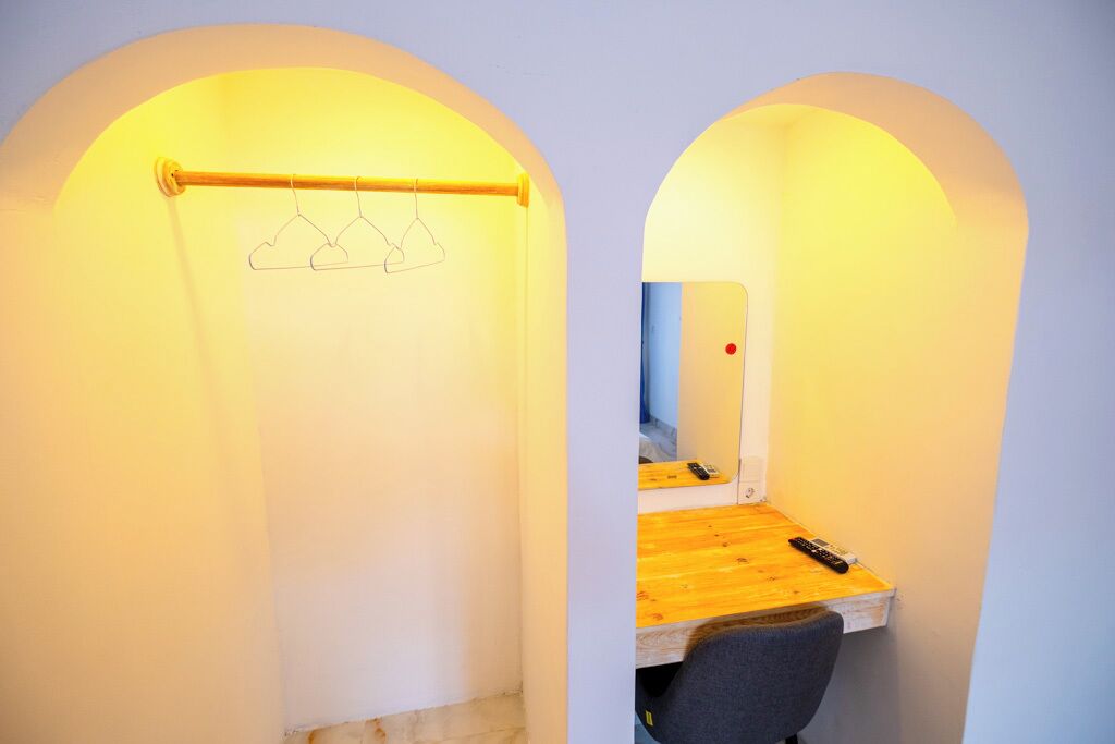 A small, cozy room with a wooden desk, a chair, and a hanging clothes rack.