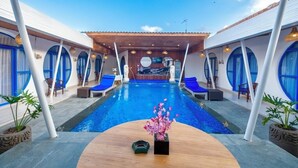 A pool area with blue-framed windows, lounge chairs, and a central table with a flower arrangement. - Anny Guesthouse 2 by Ecommerceloka (Denpasar)