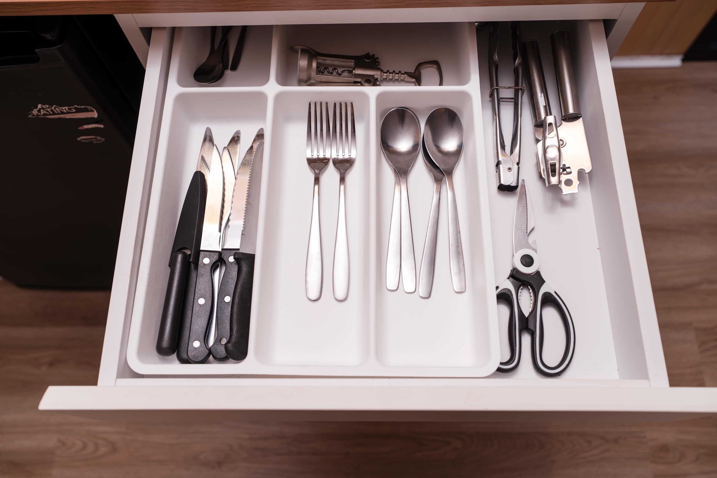 Un tiroir contenant divers ustensiles de cuisine, notamment des couteaux, des fourchettes, des cuillères et des ciseaux.