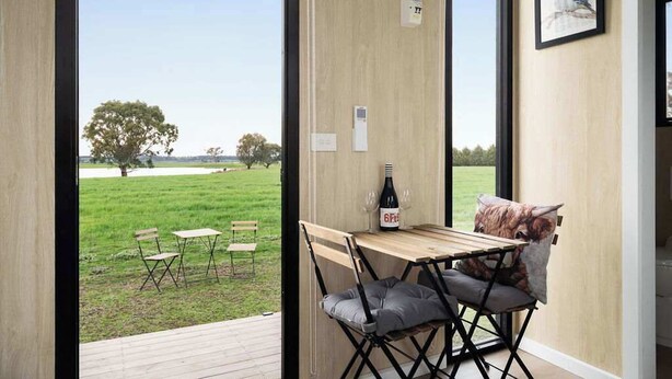 Une pièce avec une table et des chaises en bois, une bouteille de vin et un tableau encadré au mur.