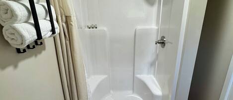 A modern shower room with a glass door, a towel rack with folded towels, and a wooden floor.