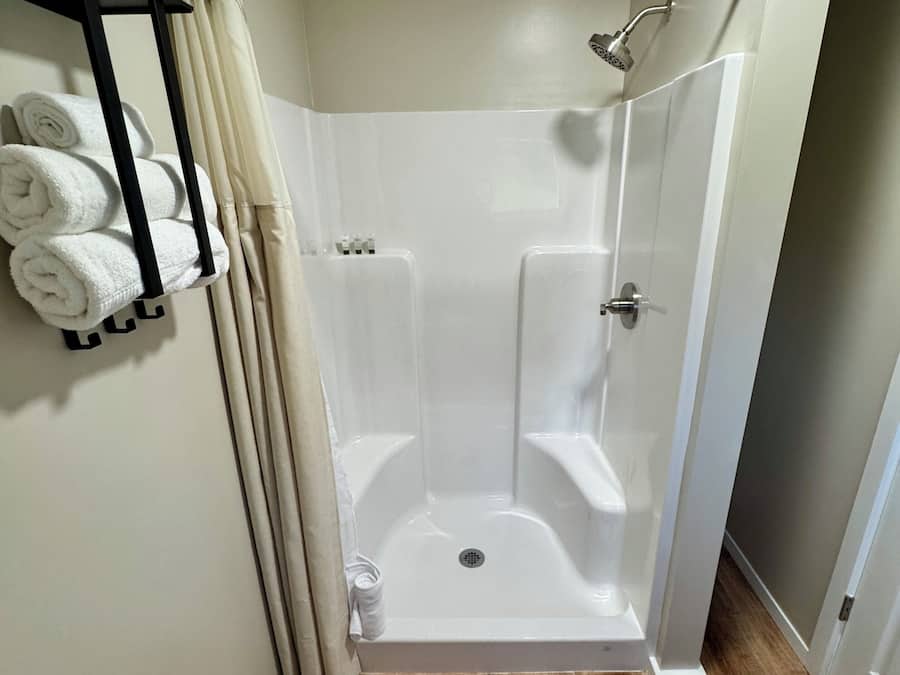 A modern shower room with a glass door, a towel rack with folded towels, and a wooden floor.