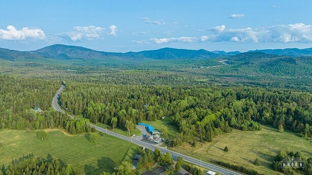 An aerial view of a rural area with a road, a blue building, and surrounding forested landscape.