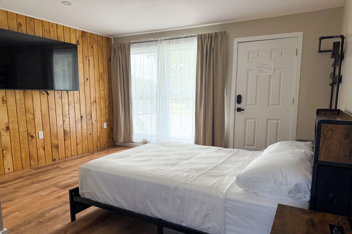 Habitación de hotel con pared de paneles de madera, cama con ropa blanca, televisor montado sobre la cama y una puerta con un cartel.