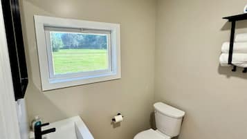 Un baño con ventana, inodoro, lavamanos y perchero para toallas.