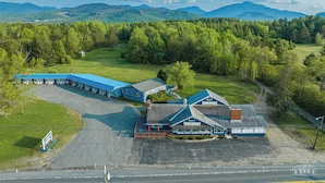 A motel with a blue roof, a parking lot, and a view of the surrounding forest and mountains.