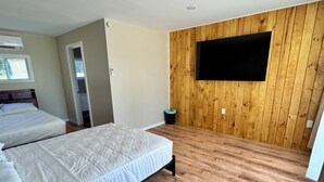 A bedroom with two beds, wooden flooring, a mounted TV, and a window.
