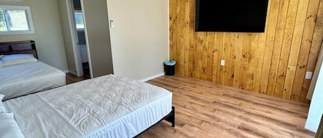 Ein Schlafzimmer mit zwei Betten, Holzboden, einem Wandfernseher und einem Fenster.